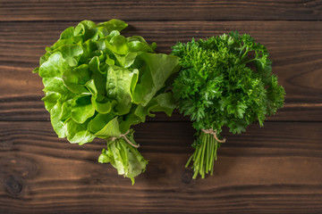A bunch of parsley and a bunch of lettuce on a wooden table. Flat lay.