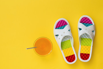 Orange drink and slates with colorful soles on yellow background. The concept of summer vacation. Flat lay.