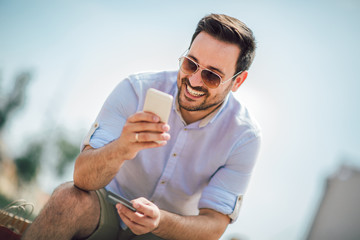 Cheerful young casual man holding mobile phone and credit card outdoor