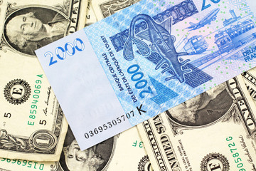 A close up image of a blue, two thousand, West African franc bank note in macro on a background of United States one dollar bills