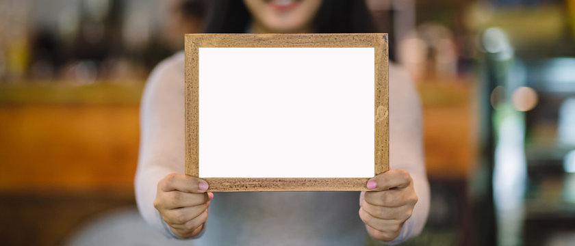 woman holding blank wooden frame in coffee shop