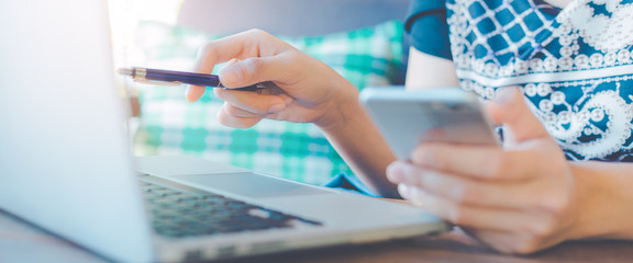 Woman's hand is using a pen pointing to the computer and mobile phone.