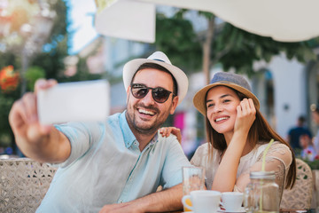 Beautiful loving couple sitting in a cafe enjoying in coffee and make selfie photo