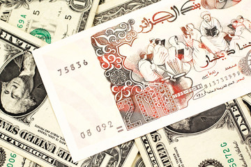 A macro image of a beige two hundred Algerian dinar bank note on a background of American one dollar bills