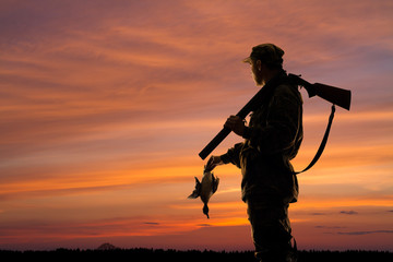 hunter with downed duck at sunset
