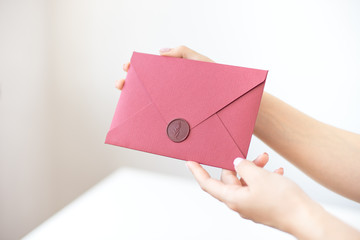 Close-up photo of female hands holding a silver invitation envelope with a wax seal, a gift certificate, a postcard, a wedding invitation card