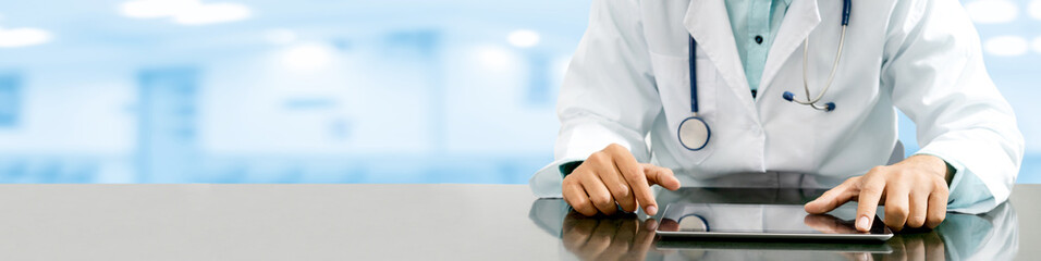 Male doctor sitting at table with tablet computer in hospital office. Medical healthcare staff and...