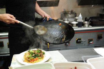 Close up of chef plating the noodle on to a plate from a wok