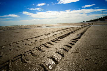 Off road car tyre track on sandy beach, with ocean and blue sky as blurred background