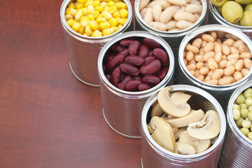 Canned green peas, beans, corn, olives and mushrooms in tin cans. Preserved food on wooden table