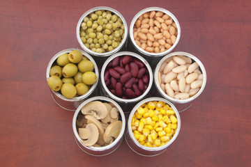 Seven tin cans with canned food on wooden background, top view