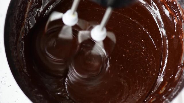Mixing chocolate dough or batter for baking cakes, cookies, pastry. Mixer beating chocolate in bowl. Closeup view footage