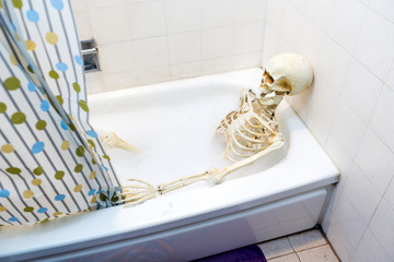 Bony skeleton taking a bubble bath in a grungy off-white dirty tub