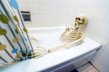Bony skeleton taking a bubble bath in a grungy off-white dirty tub