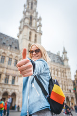 Young happy cheerful woman showing thumb up against the backdrop of the Grand Place in Brussels, Belgium