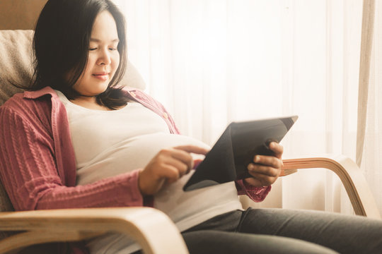 Pregnant woman feeling happy at home while taking care of her child. The young expecting mother holding baby in pregnant belly. Maternity prenatal care and woman pregnancy concept.
