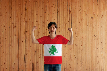 Man wearing Lebanon flag color of shirt and standing with raised both fist on the wooden wall background.