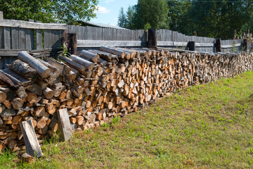 Chopped firewood stacked in a woodpile near the fence in the village