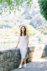 Fototapeta premium Summer photo shoot on the streets of Kotor, Montenegro. Beautiful girl in white dress and hat.