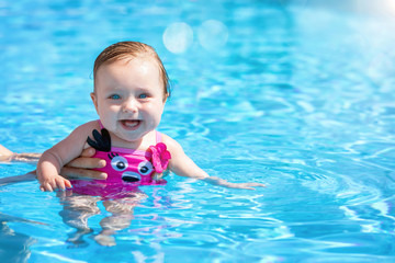 Fototapeta na wymiar Happy, cute baby girl enjoys a hot summer day in the blue waters of a swimming pool