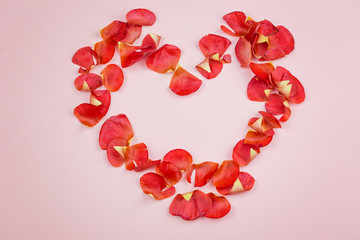 Heart of red petals on a light pink background. Space for text