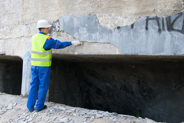 a city worker, wearing a white helmet, cleans the walls from graphics and writing, with a metal brush, before painting