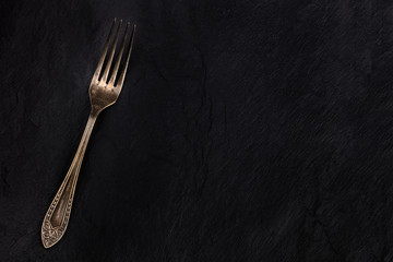 A vintage fork on a black background, shot from the top with a place for text, an abstract food...