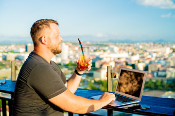 male talking on the phone and working on a laptop in a rooftop cafe with a panoramic view. man...