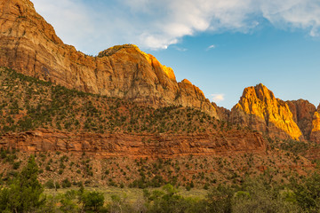 A landscape view of the amazing rugged landscape from the canyon floor at Zion National Park, USA against a beautiful bright blue sky and moon in the distance