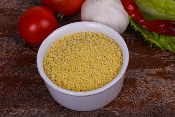 Raw couscous in the bowl served salad leaves, tomato and pepper