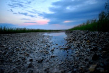 Puddle on gravel road with dusk lit sky