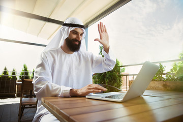 Arab saudi businessman working online with a laptop and tablet in a coffee shop or a cafe with an...