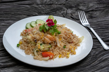 Fried rice with shrimps and vegetables in a white dish on an old wooden table, close up . Thai food , Thai cuisine