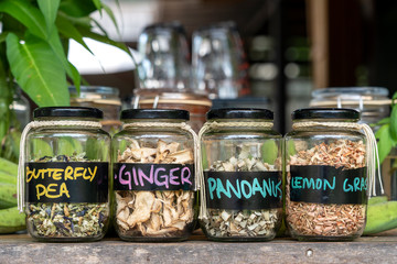Assortment of dried spices in glass bottles on wooden background. Dry ginger, pandanus, lemon grass and butterfly pea in glass jars, closeup