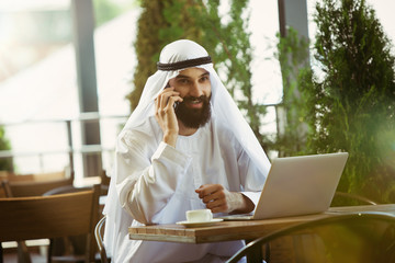 Arab saudi businessman working online with a laptop and tablet in a coffee shop or a cafe with an...