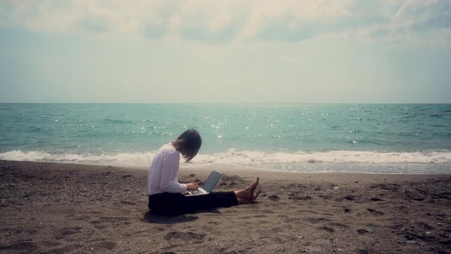 successful business woman with a mobile phone working in a laptop sitting on the beach. concept - vacation. toned image.