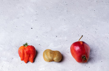 Three ugly fruits: strawberry, kiwi and apple on grey concrete background. 