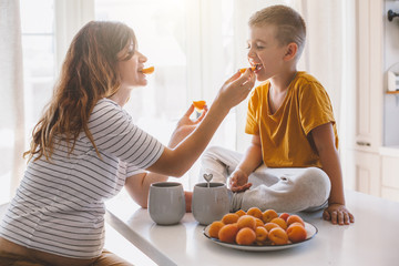 Pregnant mom with kid eating fruits together in the kitchen
