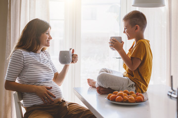 Pregnant mom with kid drinking tea together in the kitchen
