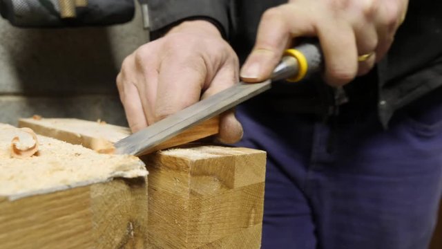 Ten-second video of a mans hand using a carpenters chisel tool to carve a pieces of wood.