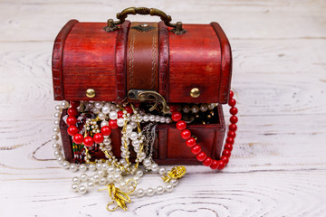 Vintage treasure chest full of jewelry and accessories on white wooden background