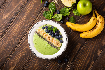 Breakfast detox green smoothie bowl from banana and spinach on wooden background. Healthy food concept with copy space, top view