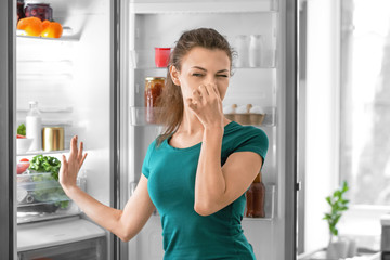 Young woman feeling bad smell from refrigerator in kitchen