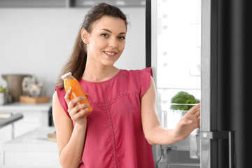 Woman with bottle of juice standing near open fridge at home