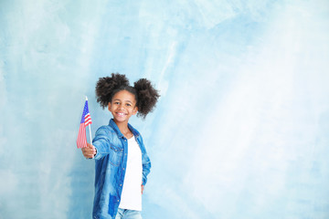 Cute African-American girl with national flag of USA on color background