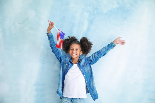 Cute African-American girl with national flag of USA on color background