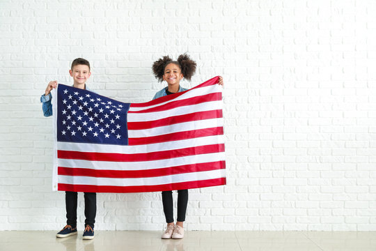 Cute children with national flag of USA near white brick wall