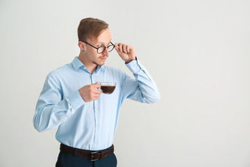 Handsome businessman with cup of coffee on light background