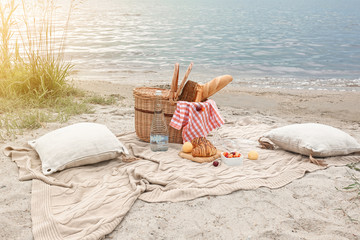 Wicker basket with tasty food and drink for romantic picnic near river - obrazy, fototapety, plakaty