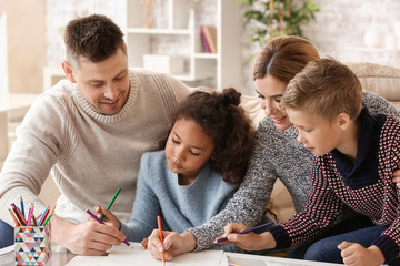 Happy couple with little adopted children drawing at home